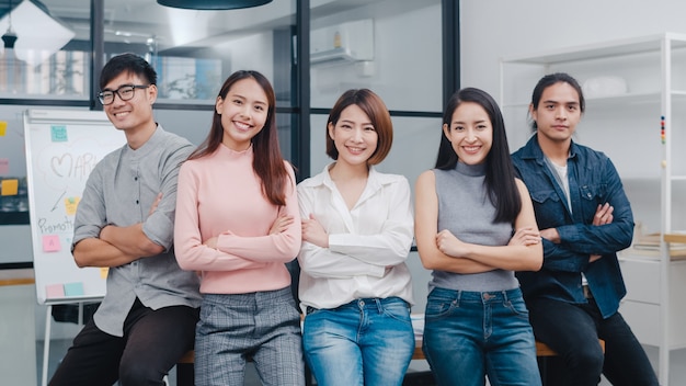 Group of asia young creative people in smart casual wear smiling and arms crossed in creative office workplace. Free Photo
